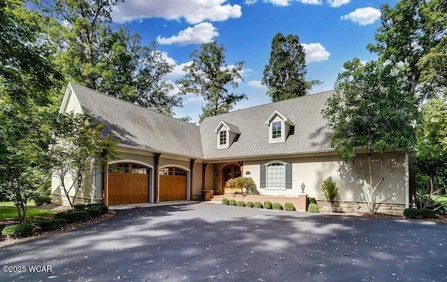 cape cod house featuring an attached garage, driveway, and stucco siding