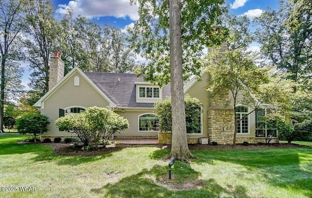rear view of house with a lawn, stucco siding, stone siding, and a chimney
