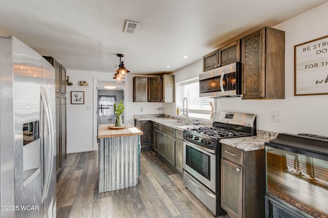 kitchen with appliances with stainless steel finishes, pendant lighting, wood-type flooring, sink, and dark brown cabinetry