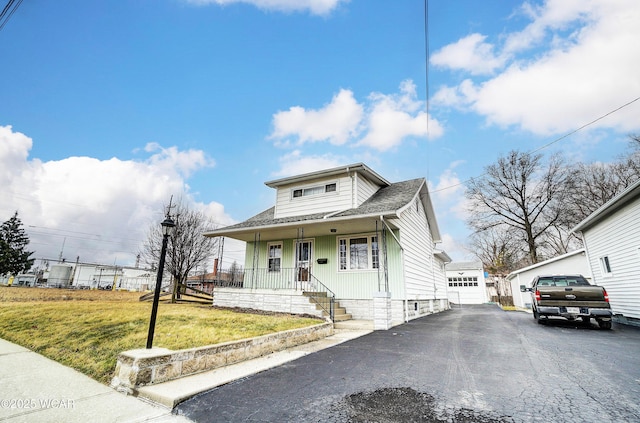 bungalow with an outbuilding, aphalt driveway, covered porch, a shingled roof, and a front yard