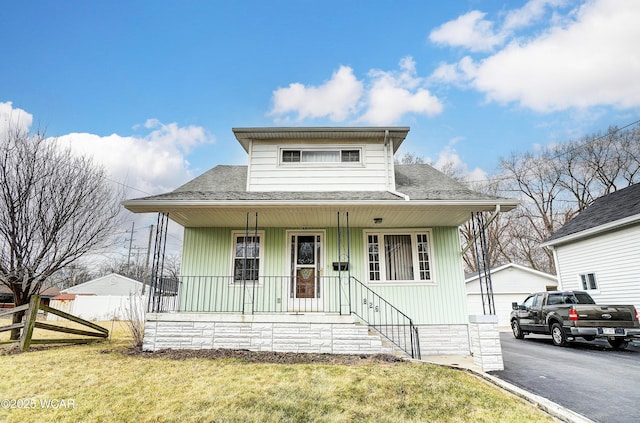 bungalow-style house with a shingled roof, covered porch, fence, an outdoor structure, and a front lawn