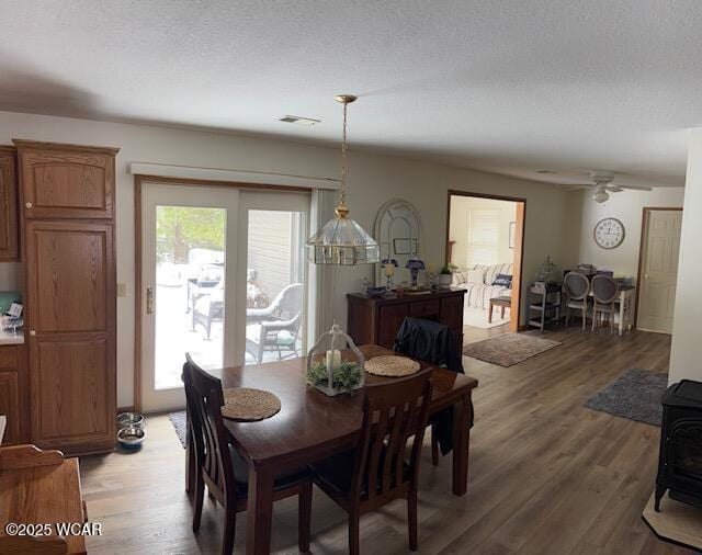 dining room with visible vents, a wood stove, ceiling fan, a textured ceiling, and wood finished floors