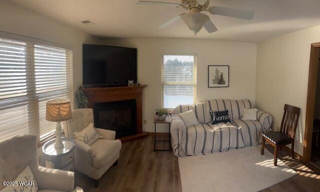 living area with a fireplace with raised hearth, visible vents, dark wood-style flooring, and a ceiling fan