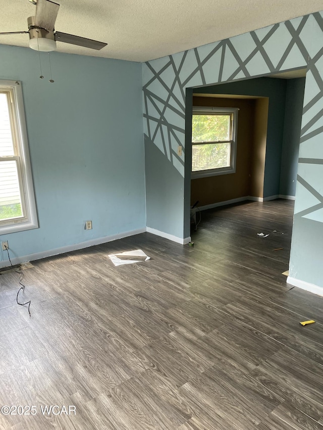 empty room with ceiling fan, a healthy amount of sunlight, dark wood-type flooring, and a textured ceiling