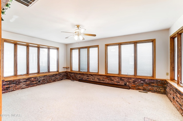 empty room with carpet flooring, a baseboard heating unit, ceiling fan, and brick wall