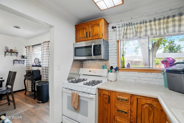 718 Wildwood Ave, Lima, OH 45807 - kitchen featuring stainless steel microwave, white gas range oven, decorative backsplash, light countertops, and light wood-style floors
