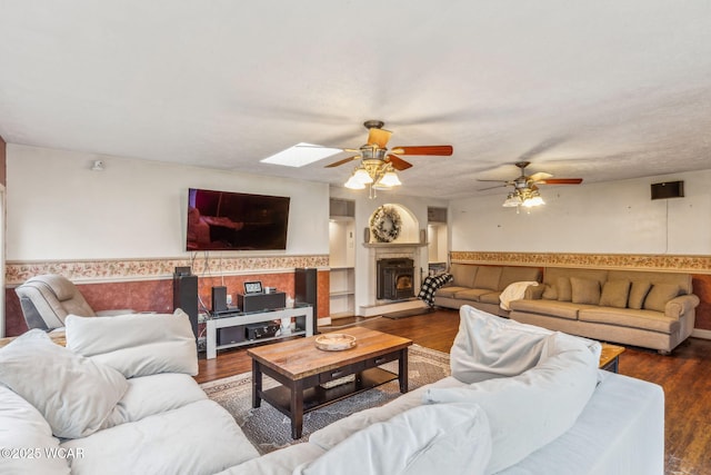 living room featuring dark wood-type flooring, ceiling fan, and a skylight