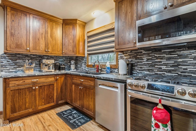 kitchen featuring appliances with stainless steel finishes, light hardwood / wood-style floors, sink, and dark stone countertops