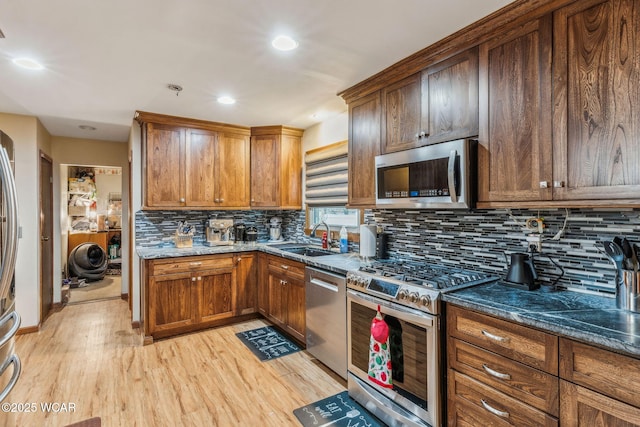 kitchen featuring dark stone countertops, sink, light hardwood / wood-style floors, and appliances with stainless steel finishes