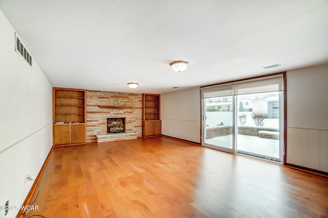 unfurnished living room featuring built in shelves, visible vents, a fireplace, and wood finished floors