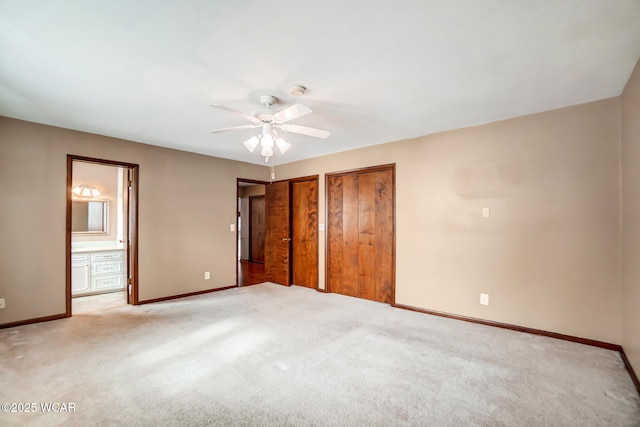 unfurnished bedroom with light carpet, baseboards, two closets, and ensuite bathroom