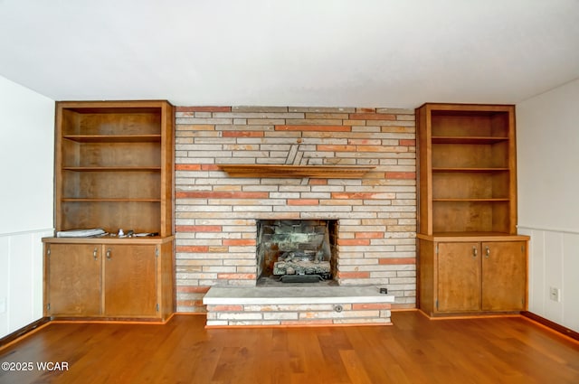 unfurnished living room with dark wood-style floors, a wainscoted wall, a stone fireplace, and built in features