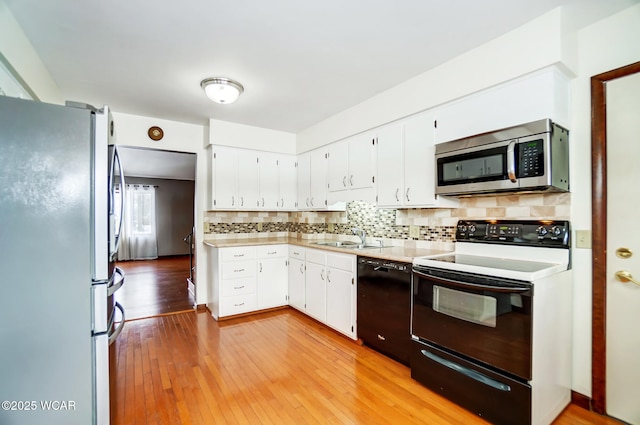 kitchen featuring tasteful backsplash, white cabinets, light countertops, black appliances, and a sink