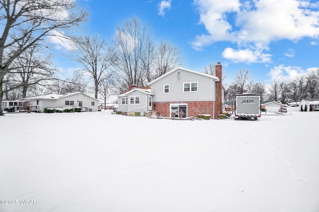 view of snowy exterior featuring a chimney, a residential view, and brick siding