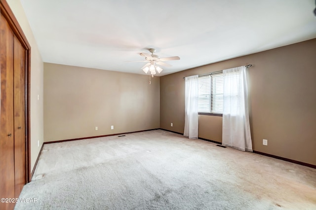 empty room with baseboards, a ceiling fan, and light colored carpet