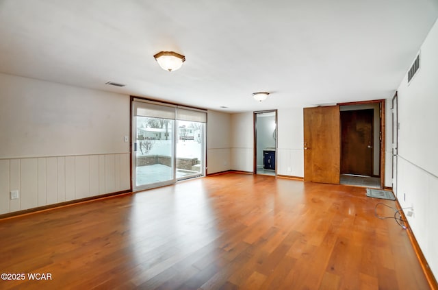 interior space with a wainscoted wall, access to outside, visible vents, and wood finished floors