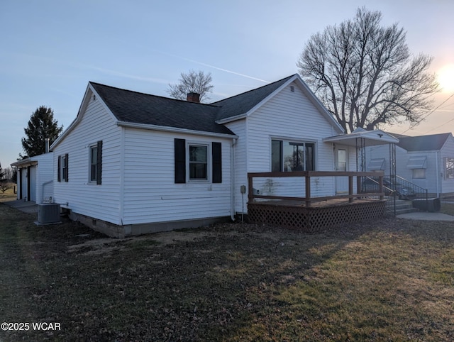 back of property at dusk with a wooden deck, a chimney, a yard, and roof with shingles