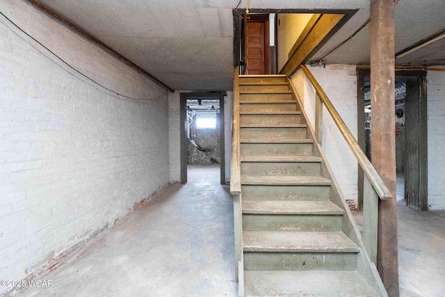 staircase with concrete flooring and brick wall