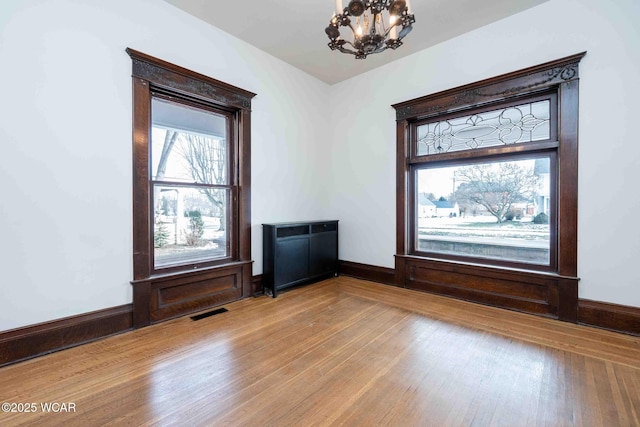 unfurnished room with a chandelier and light wood-type flooring