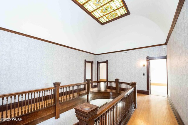 hall with ornamental molding, a towering ceiling, and light wood-type flooring