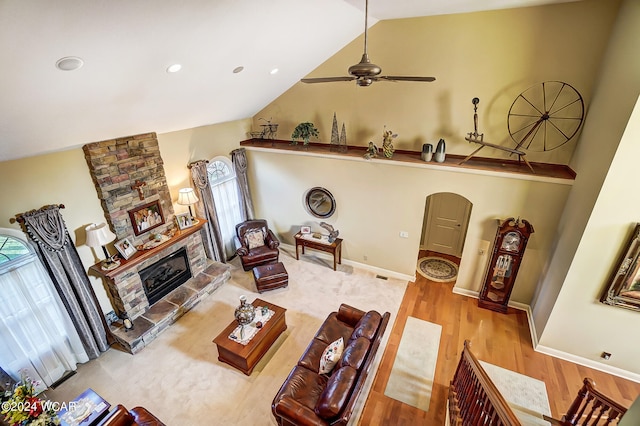 living room with baseboards, lofted ceiling, ceiling fan, wood finished floors, and a stone fireplace