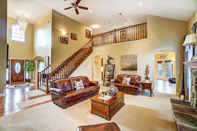 living area featuring arched walkways, a stone fireplace, visible vents, a towering ceiling, and stairs