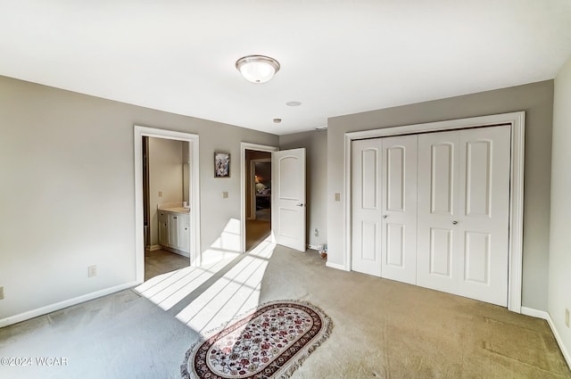 unfurnished bedroom with baseboards, a closet, ensuite bathroom, and light colored carpet