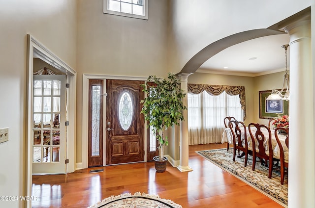 foyer entrance with arched walkways, wood finished floors, visible vents, a towering ceiling, and decorative columns