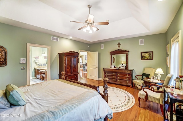 bedroom featuring visible vents, a raised ceiling, wood finished floors, and ensuite bathroom