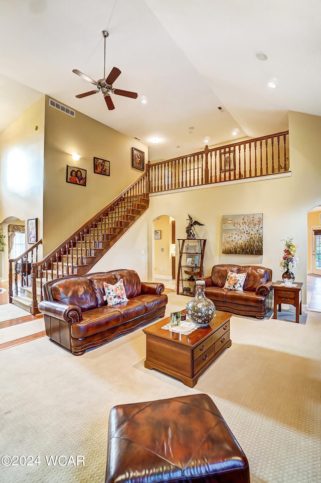 carpeted living area with arched walkways, ceiling fan, a high ceiling, visible vents, and stairway