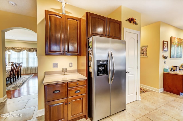 kitchen featuring stainless steel fridge, arched walkways, baseboards, light countertops, and light tile patterned flooring