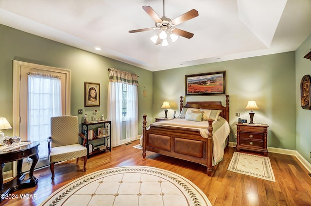 bedroom with ceiling fan, a raised ceiling, wood finished floors, and baseboards