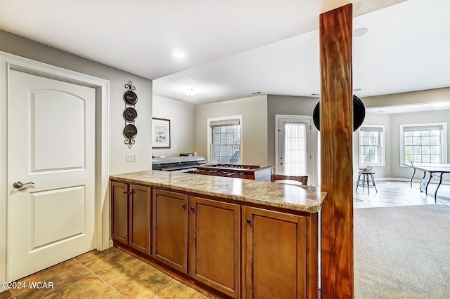 kitchen featuring light stone counters, light colored carpet, recessed lighting, a peninsula, and brown cabinetry