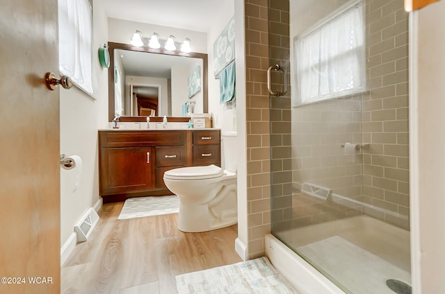 bathroom featuring wood-type flooring, tiled shower, vanity, and toilet