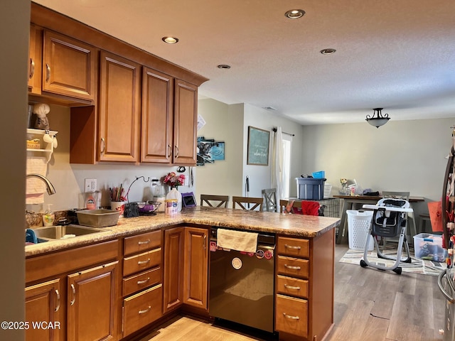 kitchen with light wood finished floors, brown cabinetry, a peninsula, a sink, and stainless steel dishwasher