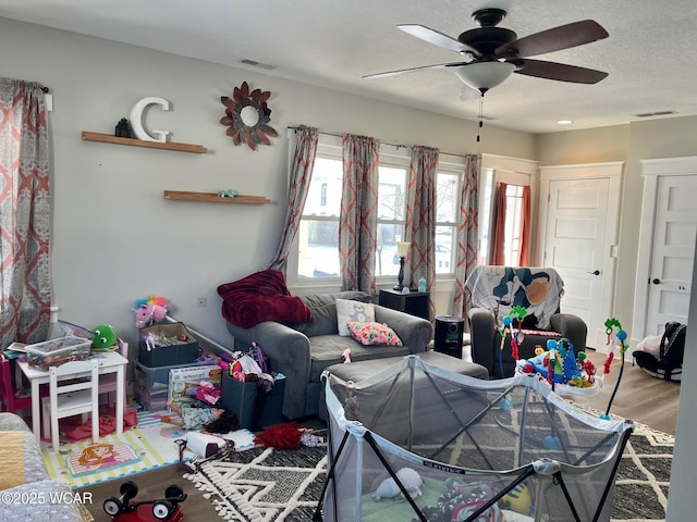 living area with a textured ceiling, ceiling fan, wood finished floors, and visible vents