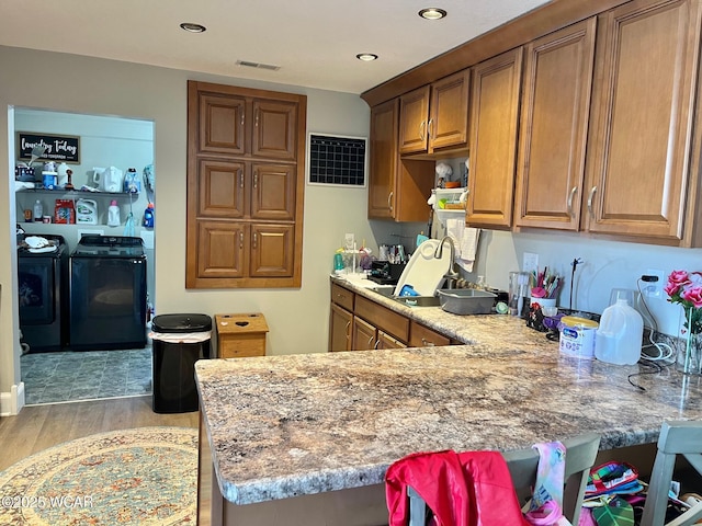 kitchen featuring light wood-style floors, washing machine and dryer, light stone counters, and brown cabinets