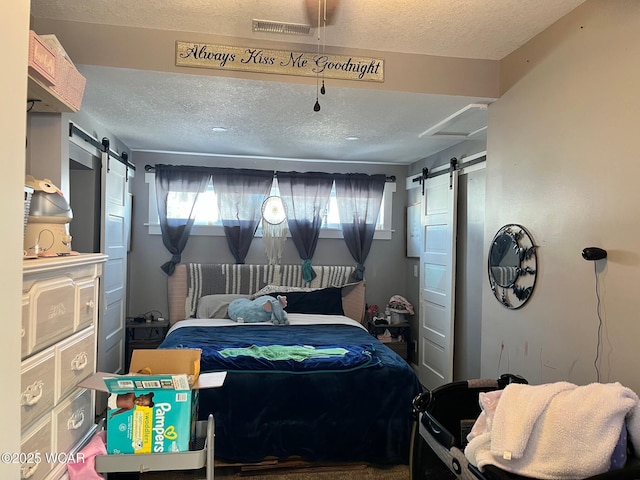 bedroom with a barn door, visible vents, and a textured ceiling