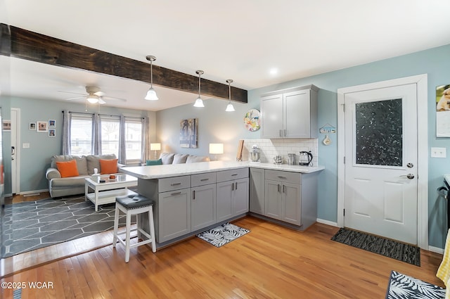 kitchen with gray cabinets, a breakfast bar, pendant lighting, decorative backsplash, and kitchen peninsula