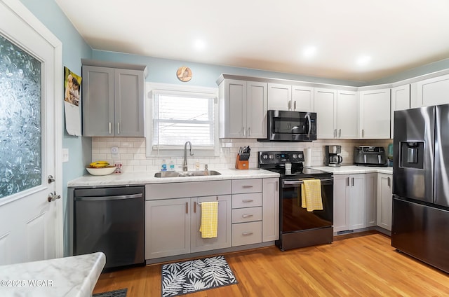 kitchen featuring sink, gray cabinetry, light hardwood / wood-style flooring, stainless steel appliances, and decorative backsplash