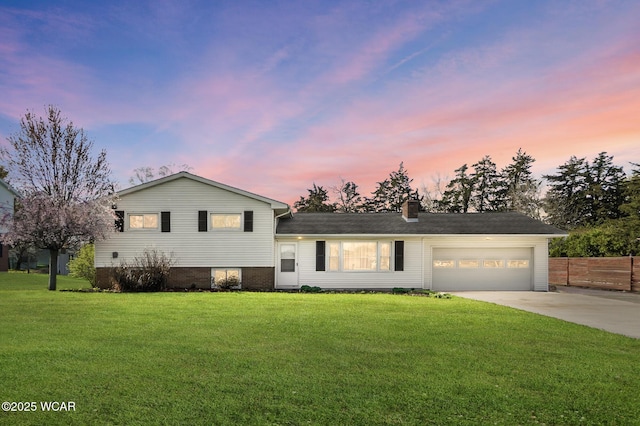 split level home featuring concrete driveway, a chimney, an attached garage, fence, and a front yard