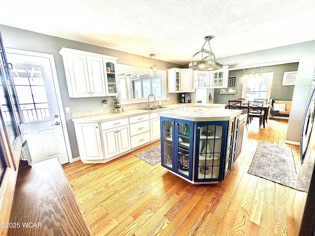 kitchen featuring pendant lighting, sink, white cabinets, a kitchen island, and light wood-type flooring