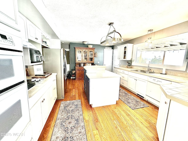 kitchen featuring pendant lighting, sink, white appliances, a center island, and white cabinets