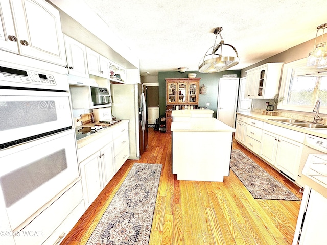 kitchen with sink, white cabinetry, decorative light fixtures, a kitchen island, and white appliances