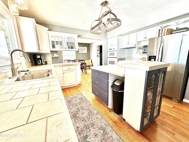 kitchen with sink, white cabinetry, stainless steel fridge with ice dispenser, a kitchen island, and pendant lighting