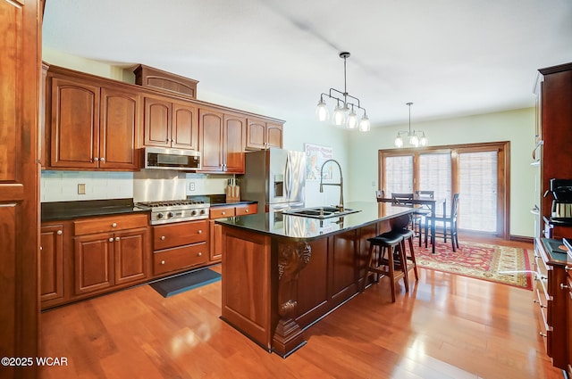 kitchen with sink, appliances with stainless steel finishes, a kitchen island with sink, pendant lighting, and light hardwood / wood-style floors