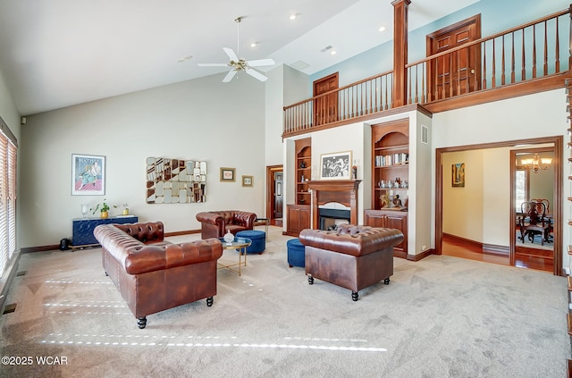 carpeted living room with a healthy amount of sunlight, ceiling fan with notable chandelier, built in features, and high vaulted ceiling