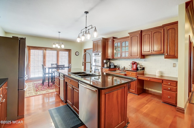 kitchen with appliances with stainless steel finishes, decorative light fixtures, sink, a center island with sink, and light wood-type flooring