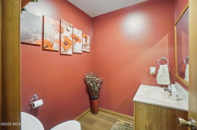bathroom featuring wood finished floors, visible vents, toilet, vanity, and baseboards