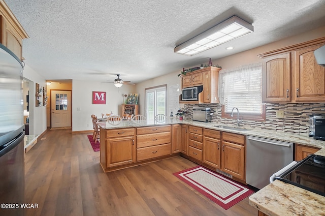 kitchen featuring stainless steel dishwasher, a sink, dark wood-type flooring, decorative backsplash, and a peninsula